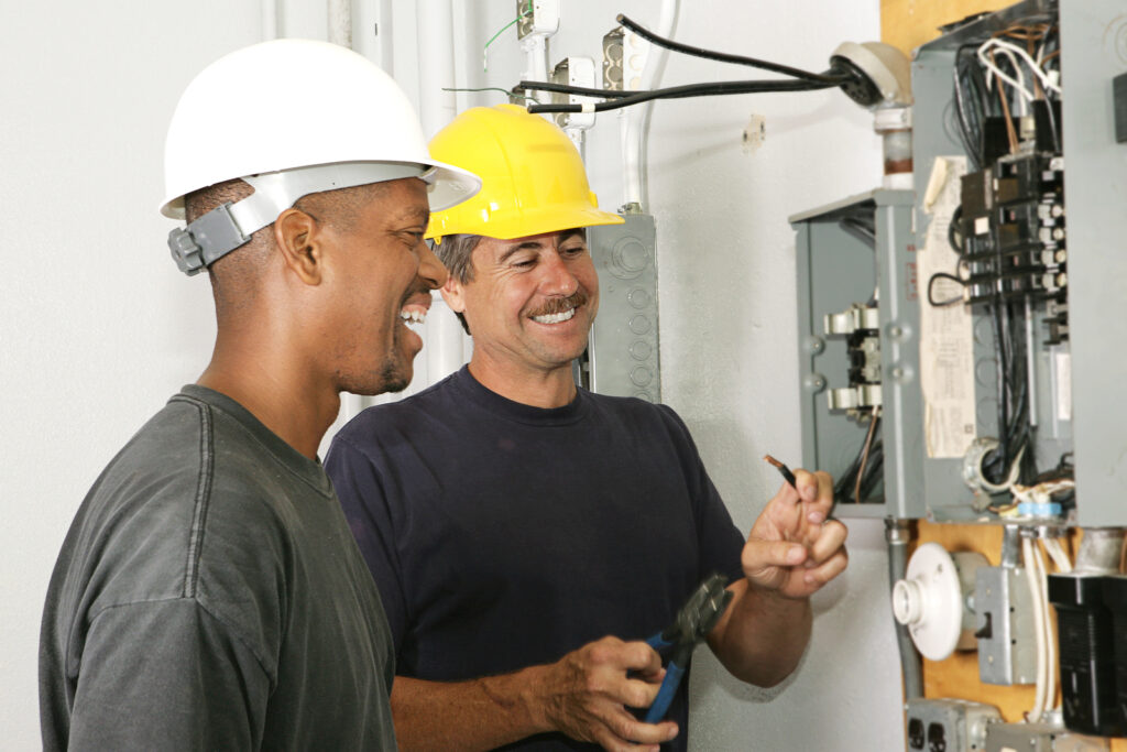 Two electricians working on an electrical panel together. Actual electricians performing work according to industry code and safety standards.